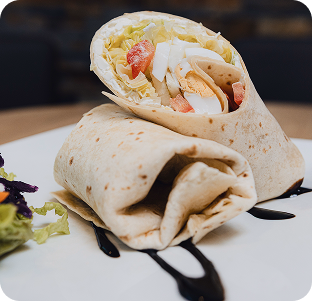 Wrap gefüllt mit Hähnchen, Gemüse und frischem Salat auf einem weißen Teller.