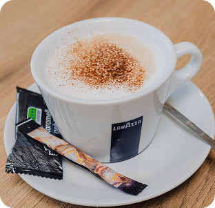Caffé Latte Macchiato in einer weißen Tasse, serviert mit Zucker und Löffel.