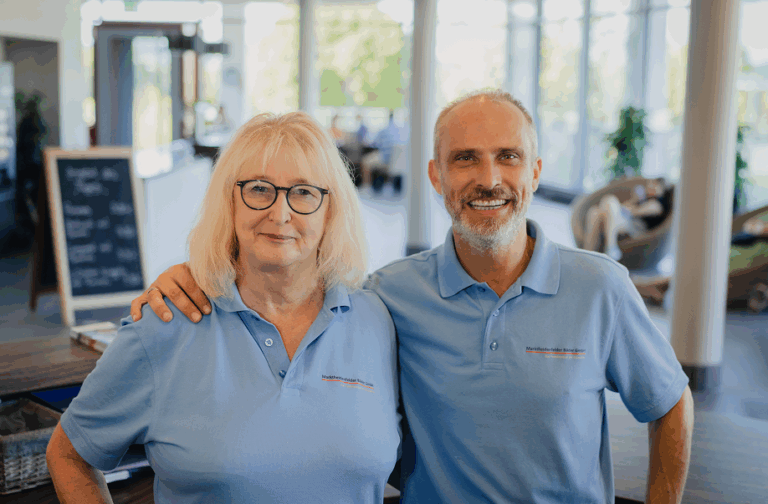 Zwei Mitarbeitende in hellblauen Poloshirts stehen lächelnd nebeneinander in einem modernen Empfangsbereich.