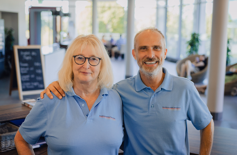 Zwei Mitarbeitende in hellblauen Poloshirts stehen lächelnd nebeneinander in einem modernen Empfangsbereich.