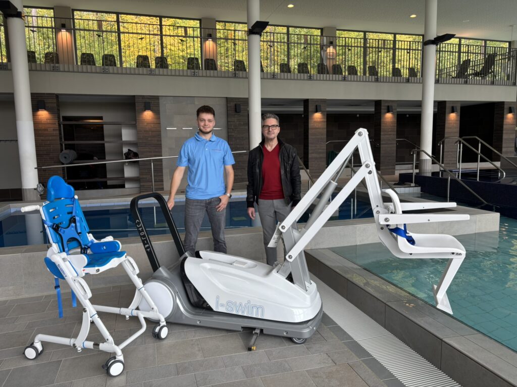 Zwei Männer in einem Schwimmbad mit einem Kinder-Duschstuhl und einem Pool-Lifter für gehbehinderte Menschen